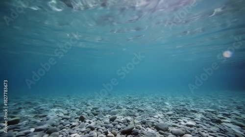 Underwater view of clear blue sea with rocky bottom and sunlight.