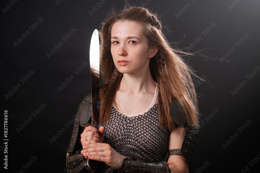 Obraz premium Portrait of a young woman, fantasy warrior in armor with a sword in her hands isolated on a dark background.