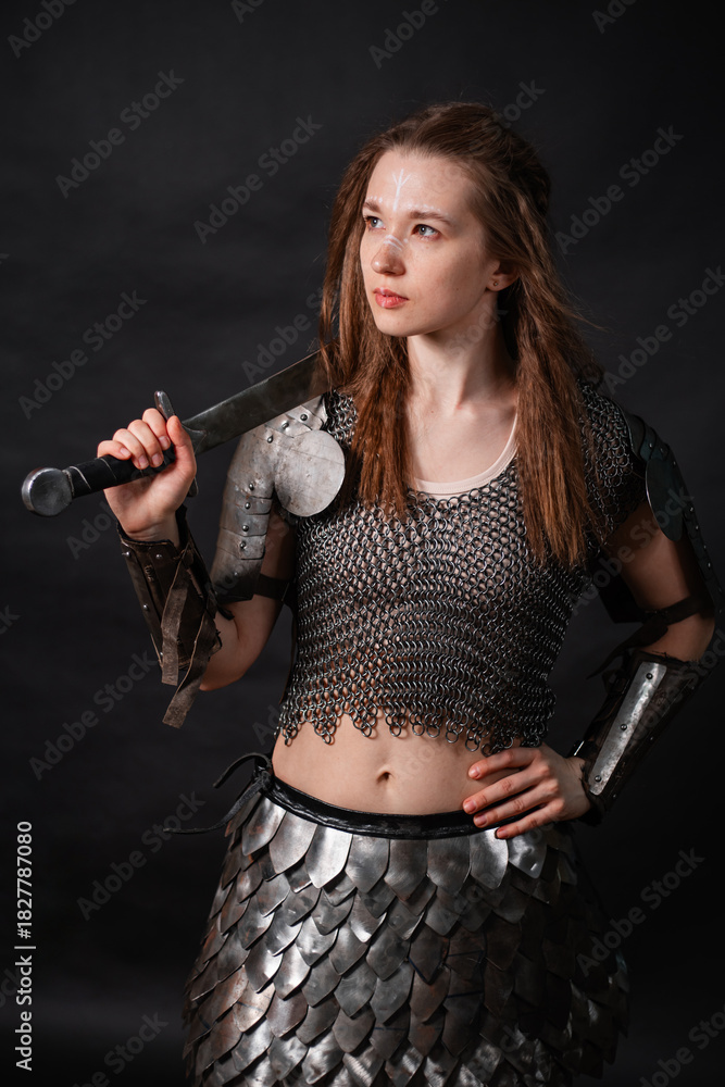 Obraz premium Portrait of a young woman, fantasy warrior in armor with a sword in her hands isolated on a dark background.