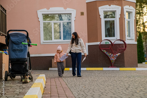 Mother Walking with Child in Urban Neighborhood Holding Drawings