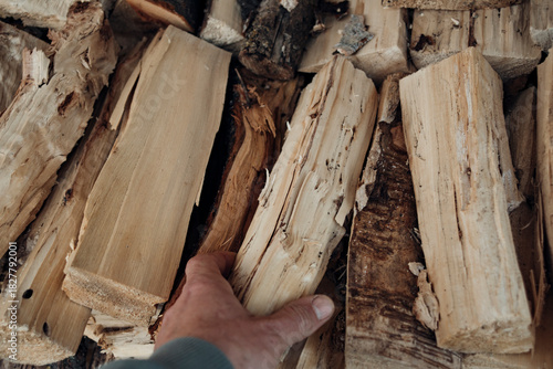 Close-up of a man's hand taking a cut and split logs from a neatly stacked pile of firewood, perfect for a cozy fireplace or outdoor fire pit