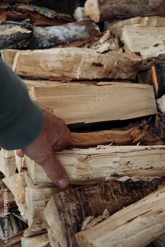 Close-up of a man's hand taking a cut and split logs from a neatly stacked pile of firewood, perfect for a cozy fireplace or outdoor fire pit