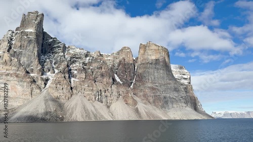 Breathtaking cliffs rise majestically above calm waters on a summer day. The clear sky showcases the beauty of the Arctic landscape with snow-capped peaks.