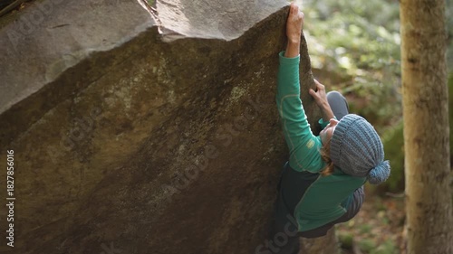 strong female climber climbs hard crag bouldering reaching holds on cliff edge showing strength and power of her fingers and forearms. healthy active leisure, rock climbing outdoors in autumn forest.