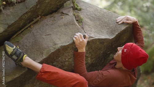 man rock climber climbs up on top of bouldering on edge of overhanging cliff. man reaching holds on slope rock surface. healthy lifestyle, active leisure. rock climbing outdoor in autumn forest.