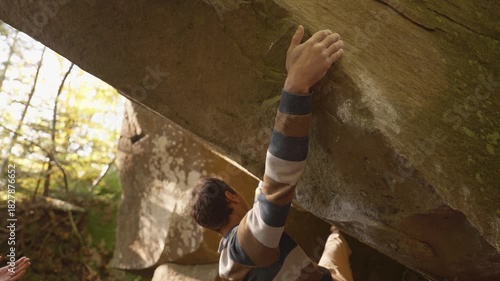 slow motion adult man rock climber climbs on overhanging cliff edges using wide hands grips, friends belay him. climbing outdoor in autumn forest on natural rocks. healthy active lifestyle
