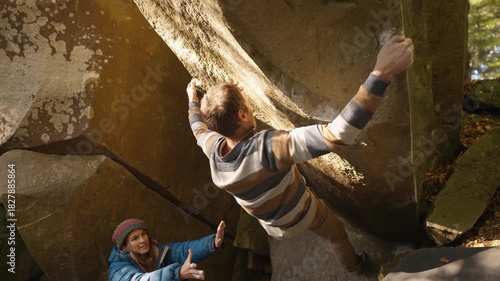 slow motion adult man rock climber climbs on overhanging cliff edges using wide hands grips, friends belay him. climbing outdoor in autumn forest on natural rocks. healthy active lifestyle