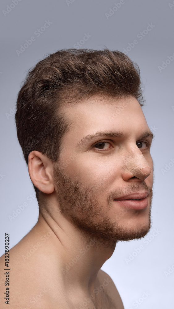 Obraz premium Man smiling slightly with nose bandage during early recovery. Concept of postoperative communication, clinic marketing, healing-stage documentation, and patient care visuals.