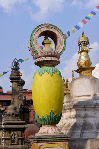 A vibrant stupa ornament stands tall against a clear blue sky at Swayambhunath, a UNESCO World Heritage Site in Kathmandu. Surrounding prayer flags flutter in the breeze
