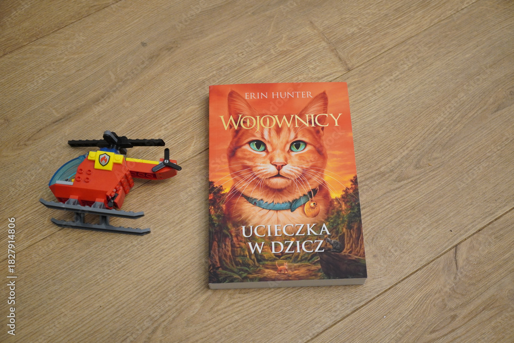 Fototapeta premium Polish edition of Warriors: Into the Wild book with a toy helicopter on wooden floor