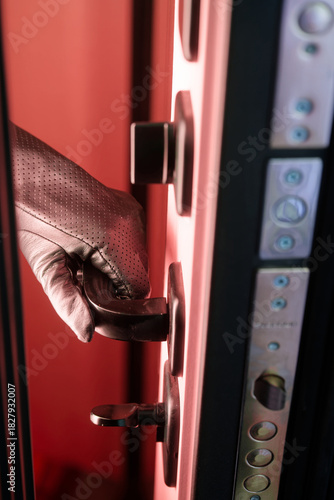 Hand in black leather glove opening armored door handle from inside with red light. Concept of illegal squatter, okupas, thief entering house, and anonymous criminal access. Photo.