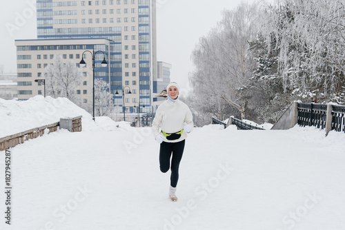 young caucasian woman running in park in winter, white sports jacket, black trousers and small waist bag on belt, active lifestyle concept, jogging in winter, sports life, copy space