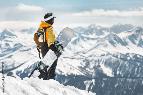 Female expert snowboarder woman is standing with snowboard in hands high in mountains outside ski slope. Backcountry and freeride concept at ski resort