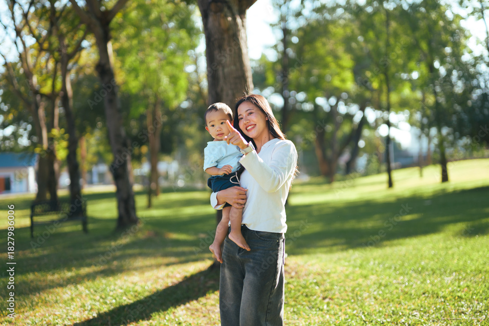 Fototapeta premium Asian mother holding son pointing in park