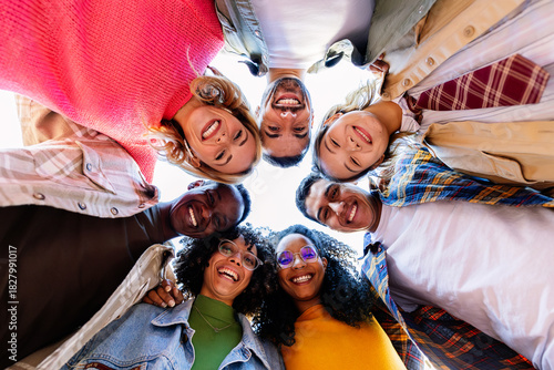 Portrait of young multiracial college student friends joining faces in circle looking at camera. Youth community and diversity concept