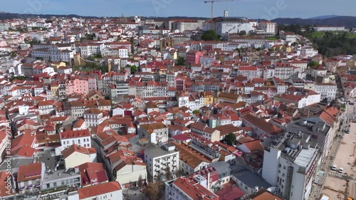 Coimbra city with orange rooftops, historic cathedral, and old buildings under clear blue sky. Aerial Shot in Portugal.