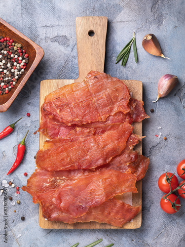 A top view of slices of dried chicken meat on a wooden tray, surrounded by various spices