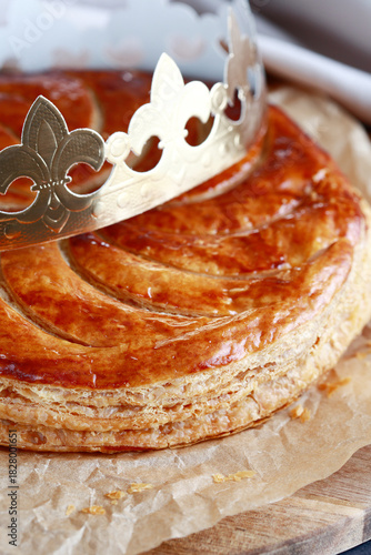 A delicious galette des rois  on a wooden board, boasting a shiny surface. A golden crown rests atop the pastry, symbolizing the celebration of epiphany with friends and family.