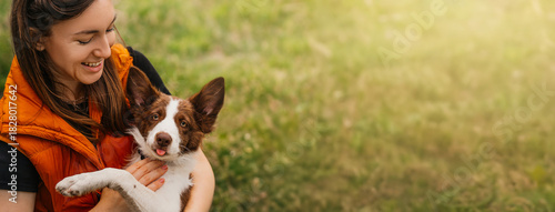 Young Woman Hugging Border Collie puppy Outdoors. A smiling young woman hugs her brown and white Border Collie dog in a green park, enjoying time together.