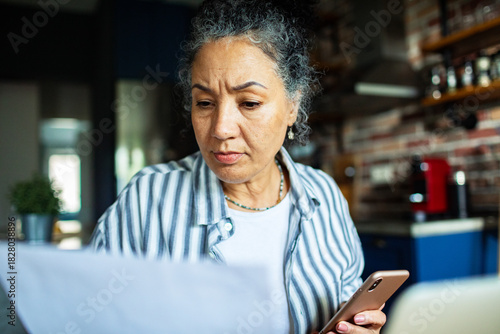 Mature woman worried reviewing bills in home kitchen