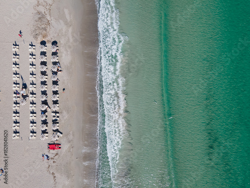 Aerial view of the beach's soft sands meeting the gentle turquoise waves, with rows of sunbeds awaiting visitors, Cala Brandinchi, San Teodoro, Sardinia, Italy.
