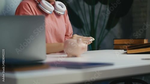 Happy teen girl putting dollars into piggy bank, saving money for her dream goal