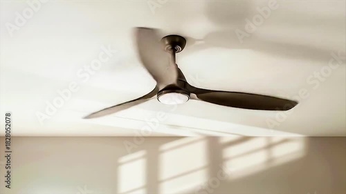 Minimal elegance in motion—sleek ceiling fan casts soft shadows across sunlit white ceiling and modern interior.