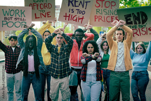 Diverse group of young protesters raising crossed arms and holding signs about rising prices, high rent and low wages during the cost of living crisis, demanding fair pay and affordable living.