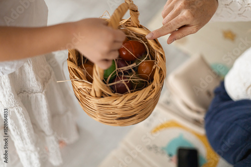 A childs hand reaches for a woven basket filled with colorful eggs. The scene captures a warm, family-oriented atmosphere at home, evoking sensory experiences.