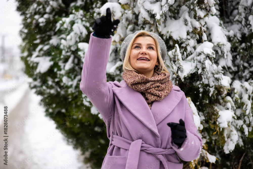 Obraz premium Snowy winter day in a park with a woman enjoying the snowfall while wearing warm clothing