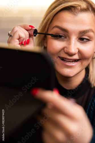 Woman applying mascara while looking in a mirror at a beauty salon during the daytime