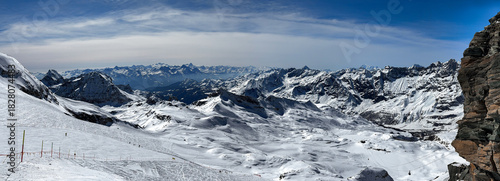 Wide panoramic view of the snowy Swiss Alps with dramatic mountain ridges, soft winter light, and untouched snowfields. High-resolution landscape capturing alpine beauty in winter.