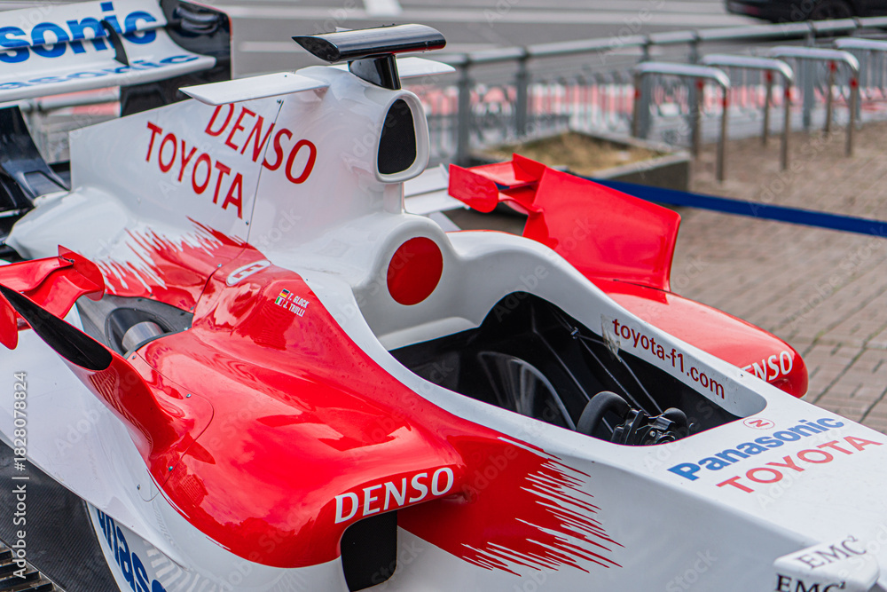 Fototapeta premium Toyota Formula 1 TF-108, vibrant red and white race car with Denso logo, viewed from angle, indoor exhibition setting, air intakes, vents, tiled floor, railing, even - Kyiv, Ukraine 10-10-2024