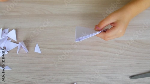 A child creating paper white snowflakes at a table at home. A child cuts patterns on paper with scissors. Decoration for the winter holiday.