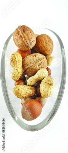 Assorted walnuts, peanuts and hazelnuts placed in a transparent glass bowl on a white background. Natural rustic snack mix for healthy lifestyle, vegan food, recipes, Christmas and autumn themes.