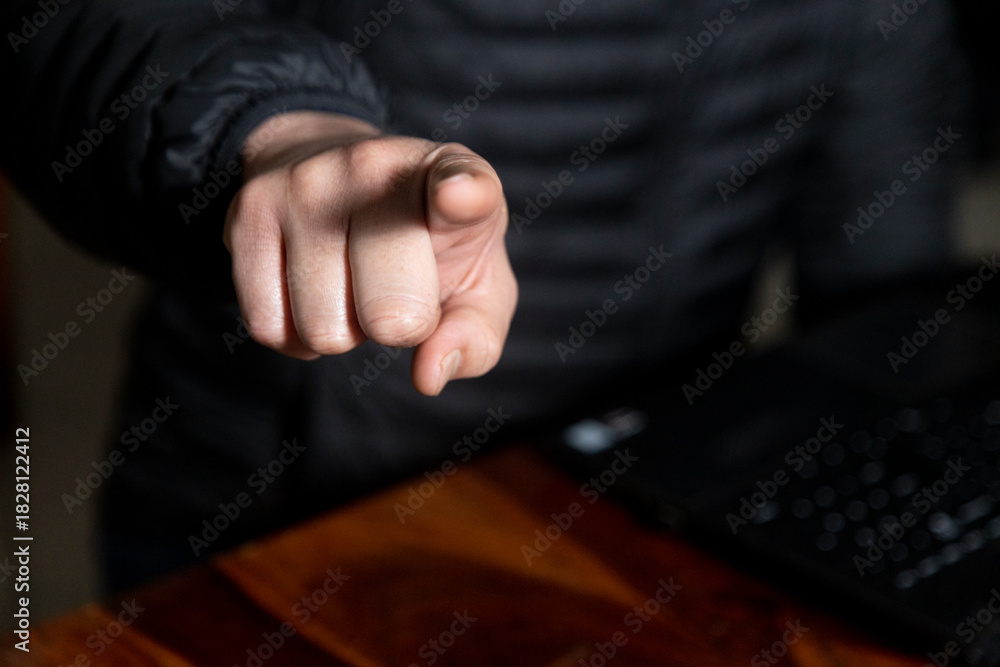 Obraz premium lose up of a man's hand working on a laptop screen and holding a mobile, wearing a black puffer jacket and gold ring. Concept of authority, accusation, or instruction in a business setting.