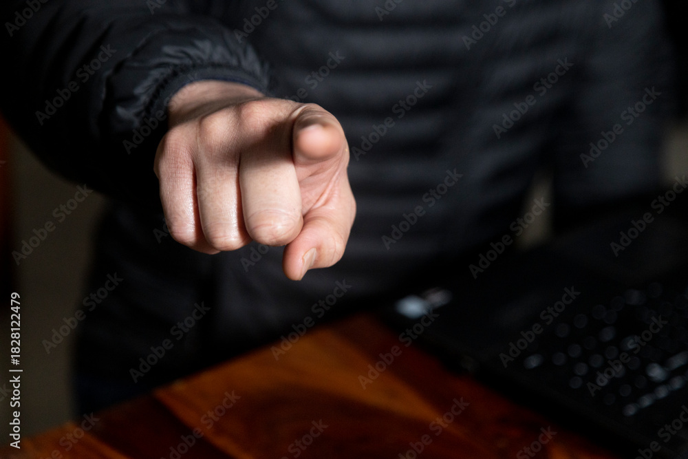 Obraz premium lose up of a man's hand working on a laptop screen and holding a mobile, wearing a black puffer jacket and gold ring. Concept of authority, accusation, or instruction in a business setting.