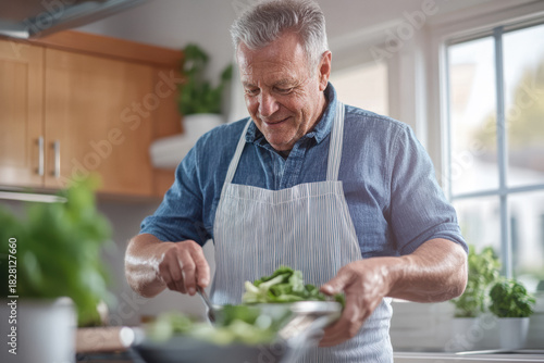 Senior man smiling as he mixes fresh green salad in a bowl in his bright home kitchen, enjoying healthy cooking, simple living and mindful food preparation for well being