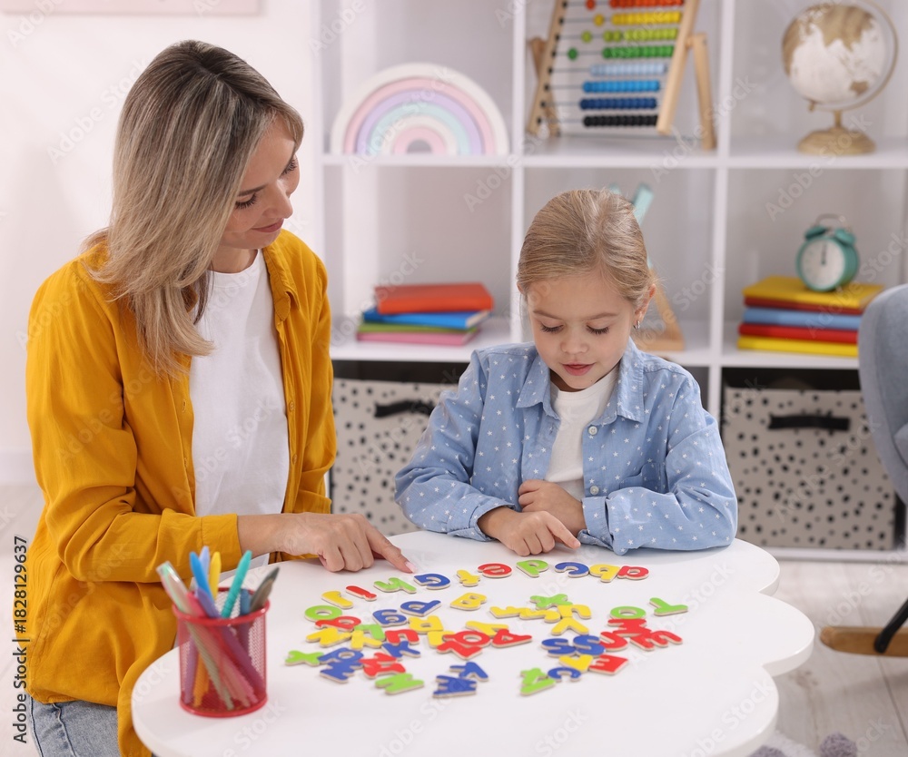 Fototapeta premium Mother teaching her daughter alphabet at white table indoors