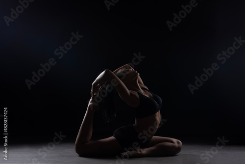 Dramatic silhouette of a woman performing an yoga . Artistic black and white studio fitness photography with rim lighting.