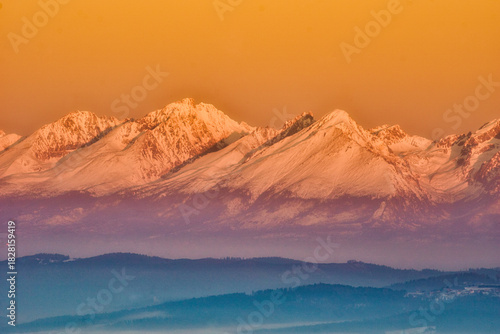 Aerial view of snow-capped peaks basking in the warm glow of the setting sun, casting long shadows over the landscape, Spisska nova Ves, Kosicky kraj, Slovakia.