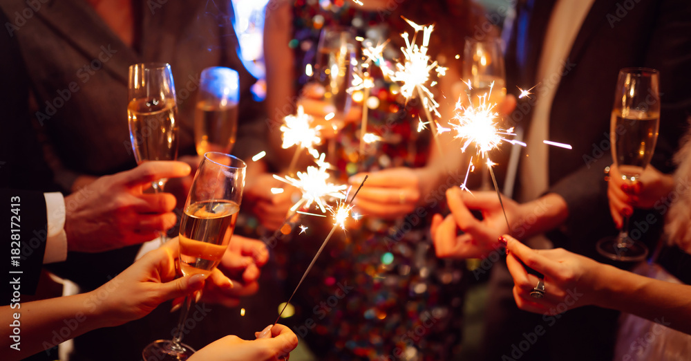 Obraz premium Hands hold sparklers, creating bright sparks in a lively setting. Friends celebrate together as lights twinkle and laughter fills the air during a special event.