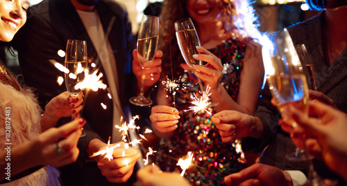 Hands hold sparklers, creating bright sparks in a lively setting. Friends celebrate together as lights twinkle and laughter fills the air during a special event.