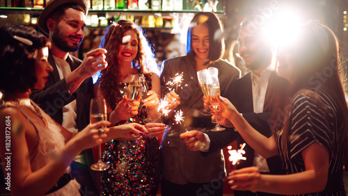 Friends gather at a vibrant bar to celebrate New Year's Eve. They enjoy drinks while holding sparklers, surrounded by a festive atmosphere and sparkling decorations.