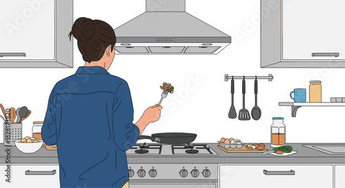 Woman seen from behind is cooking a healthy meal in a modern kitchen stirring food in a frying pan on a gas stove.