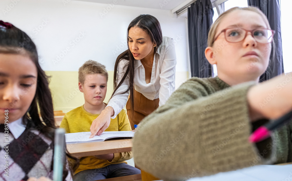 Fototapeta premium The teacher is looking over one student’s homework, giving calm guidance while checking their work. The classroom feels focused as the student waits for feedback.