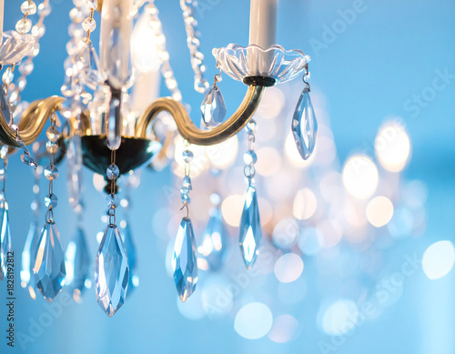 Elegant crystal chandelier details with hanging glass prisms and soft blue bokeh light, close-up of decorative lighting elements creating a bright, refined atmosphere for interiors, classic decor