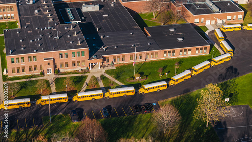 Aerial view of a typical American school with a long row of yellow school buses lined up outside the building on a sunny autumn day.