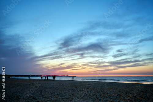 Fototapeta Naklejka Na Ścianę i Meble -  Blurred silhouettes of people walking on a sandy beach by the Baltic Sea in the evening