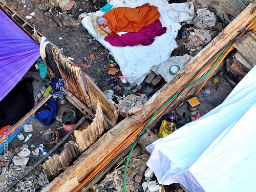 Dhaka, Bangladesh - 28 November 2025: Aerial view of the Korail slum with vibrant colored fabrics strewn across weathered rooftops, a stark contrast against the rugged landscape.